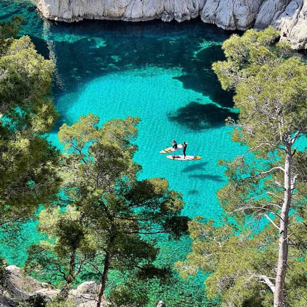 Two people stand-up paddleboarding on the translucent turquoise water of En-Vau.