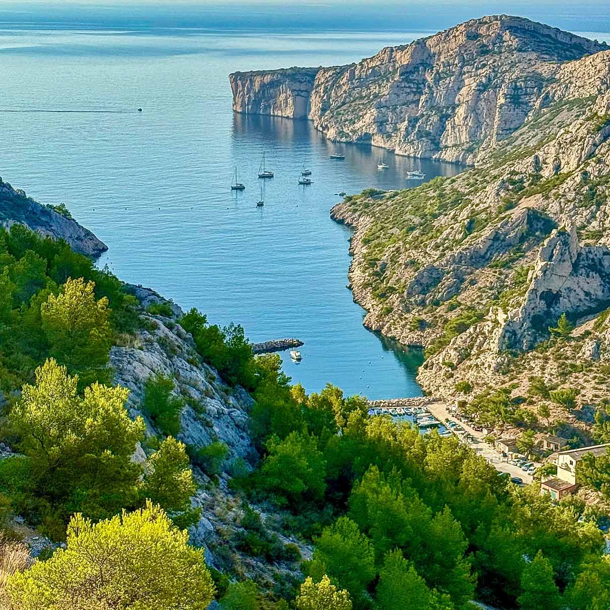 High-angle view of Morgiou harbor and its sailboats sheltered by towering cliffs.
