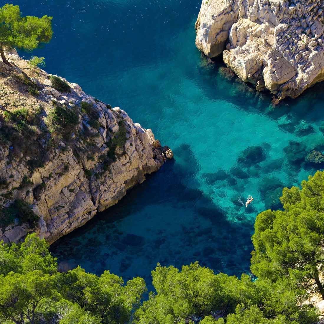 High-angle bird's-eye view of a lone swimmer in the turquoise waters of Sugiton.